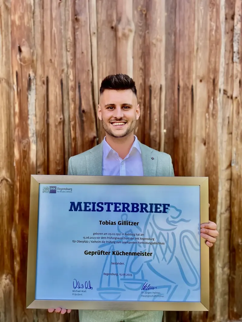 Tobias Gillitzer mit seinem Meisterbrief vor einer Holzwand